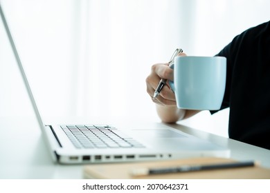 Asian Young Businessman In Relax Casual Sip A Hot Coffee In A Cup While Working In The Morning. Asian Young Man In Black Shirt Enjoy Drinking A Coffee In Morning Before Start Working.