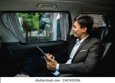 Asian Young Businessman With Tablet Sitting On Passenger Seat Of His Luxury Car