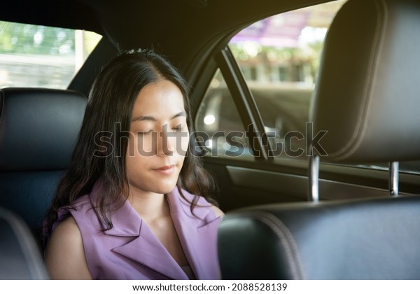 Asian young businesswoman travel by using a\
private taxi in the city, woman taking backseat in a taxi. Happy\
Asian business woman taking a seat in taxi and smiling - looking\
outside the window.