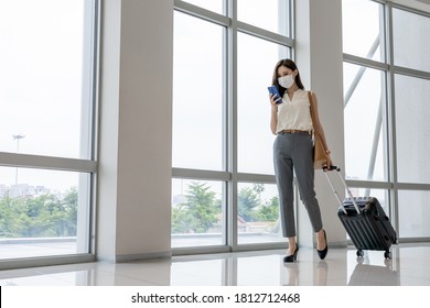 asian young businesswoman use smart phone with suitcase and wear surgical mask face protection on her business trip