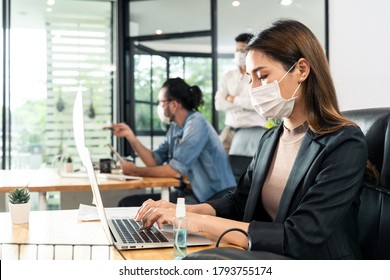 Asian Young Businesswoman Working On Computer In Office With New Normal Lifestyle Concept. Man And Woman Wear Protective Face Mask And Keep Distancing To Prevent Covid Virus After Company Reopen Again