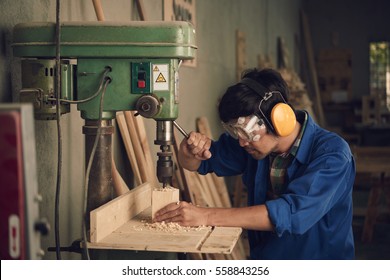 Asian young carpenter using drill press to mae hole in wooden plank - Powered by Shutterstock