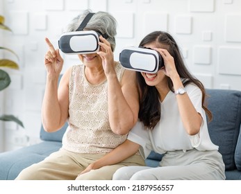 Asian young cheerful daughter wearing VR virtual reality goggles headset sitting smiling on cozy sofa in living room teaching old senior grey hair pensioner mother playing streaming 3d game online. - Powered by Shutterstock