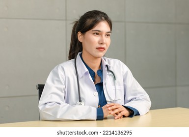 Asian Young Cheerful Happy Professional Female Practitioner Doctor In White Lab Coat Uniform With Stethoscope Sit Smiling  At Office Working Desk