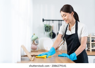 Asian young cleaning service woman worker clean kitchen table at home. Beautiful young girl housekeeper cleaner feel happy and wiping messy dirty cooking counter for housekeeping housework or chores. - Shutterstock ID 2086279141