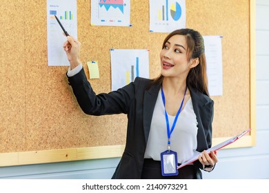 Asian Young Confident Professional Female Businesswoman Employee Staff In Formal Suit Holding Clipboard And Pen Pointing Presenting Sales Target Graph Chart Diagram Paperwork On Board In Meeting Room.