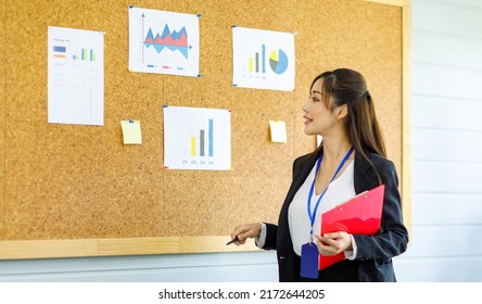 Asian Young Confident Professional Female Businesswoman Employee Staff In Formal Suit Holding Clipboard And Pen Pointing Presenting Sales Target Graph Chart Diagram Paperwork On Board In Meeting Room.