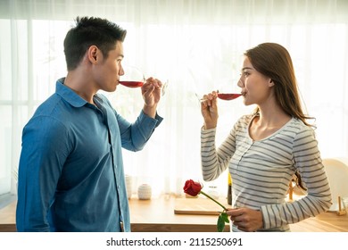 Asian Young Couple Clinking Glass Of Wine And Drink On Valentine's Day. Lovely Romance New Marriage Man And Woman Having Dinner Night Party To Celebrate Wedding Anniversary Together In Kitchen At Home