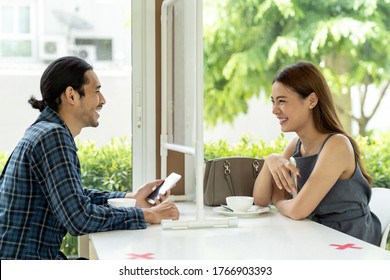 Asian Young Couple Eating Out Together At New Normal Social Distance Restaurant With Table Shield Partition Reduce Infection Of Coronavirus Covid-19 Pandemic. Restaurant New Normal Lifestyle.