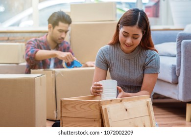 Asian Young Couple Packing The Big Cardboard Box For Moving In New House, House Hunting Concept,