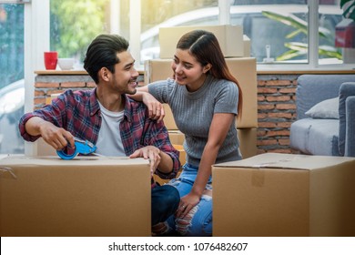 Asian Young Couple Packing The Big Cardboard Box For Moving In New Home, Moving And House Hunting Concept,