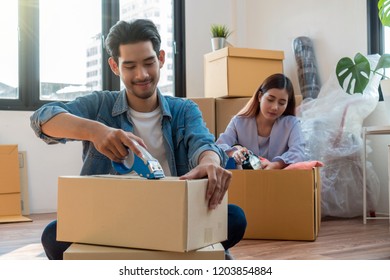 Asian Young Couple Packing Big Cardboard Box For Moving In New Home, Moving And House Hunting Concept