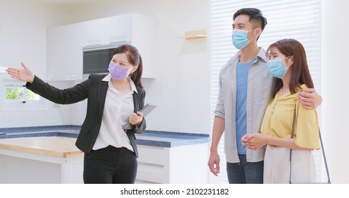 Asian Young Couple With Real Estate Agent Visiting House For Sale Or Rent - Realtor Introduces Building And They Wearing Protective Face Mask To Prevent COVID-19 At Kitchen