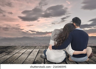 Asian Young Couple Sit And Hug Together Against The Sky In Outdoor.