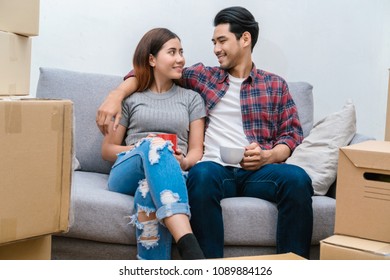 Asian Young Couple Sitting On The Sofa And Drinking For Relax After Success Packing Big Cardboard Box For Moving In New House, Moving And House Hunting Concept