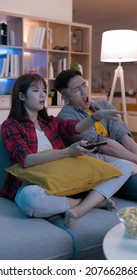 asian young couple sitting on the couch are watching tv and they feel bored in night living room at home