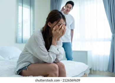 Asian young couple sitting on bed with painful after fight argument. New marriage man and woman crying and feel heartbroken for their quarrel conflict in bedroom. Family problem-separation concept.