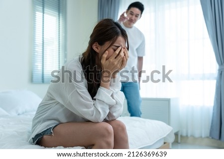 Asian young couple sitting on bed with painful after fight argument. New marriage man and woman crying and feel heartbroken for their quarrel conflict in bedroom. Family problem-separation concept.