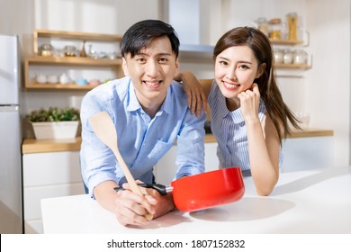 Asian Young Couple Smile To You While Cooking In The Kitchen At Home