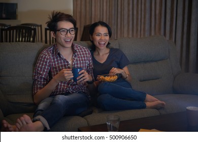 Asian Young Couple Watching Comedy Movie On Tv At Night