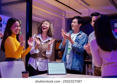 Asian young creative professional successful businesswoman staff standing greeting finishing presentation while male and female colleagues clapping hands together admire compliment in office at night. - Powered by Shutterstock