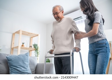 Asian young daughter support senior older man walk with walker at home. Beautiful girl help and take care of elderly mature grandpa patient doing physical therapy for health in living room in house.