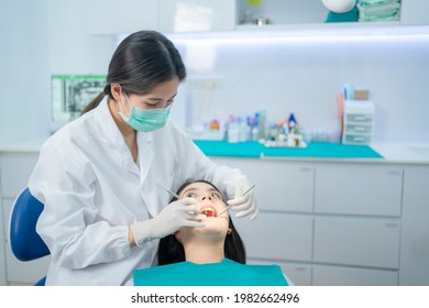 Asian Young Dentist Wearing Face Mask, Using Medical Instruments For Oral Care Check Up. Doctor Examining For Cavities And Gum Disease. Medical Occupation Service And Health Care In Dental Clinic.