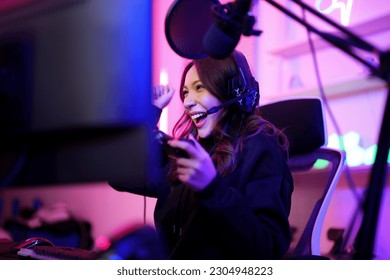 Asian young e-sport girl happy smile and fun after playing game online with her friend, then they win others competitor in neon illuminate gamer room - Powered by Shutterstock