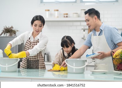 Asian Young Family Teaching Their Daughter To Clean Kitchen Counter. The Kid And Parents Dancing And Smiling Together With Fun. Happy Moment Of Lovely Family When Cleaning The House With Happiness.