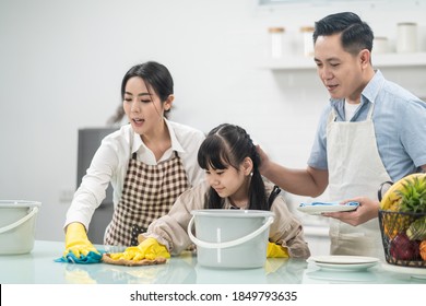 Asian young family teaching their daughter to clean kitchen counter. The kid and parents dancing and smiling together with fun. Happy moment of lovely family when cleaning the house with happiness.