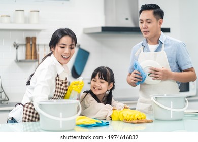 Asian Young Family Teaching Their Daughter To Clean Kitchen Counter. The Kid And Parents Dancing And Smiling Together With Fun. Happy Moment Of Lovely Family When Cleaning The House With Happiness.