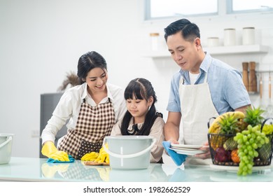 Asian Young Family Teaching Their Daughter To Clean Kitchen Counter. The Kid And Parents Dancing And Smiling Together With Fun. Happy Moment Of Lovely Family When Cleaning The House With Happiness.