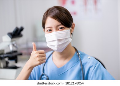 asian young female doctor who is wearing surgical face mask looks to you with thumb up gesture at the clinic - Powered by Shutterstock