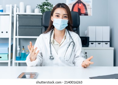 Asian Young Female Medical Doctor Talking Virtual Online With Patient. Attractive Physician Woman Wear Face Mask, Remote Work From Office Hospital And Broadcast Diagnosis Treatment To The Sick People.