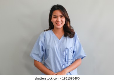 Asian Young Female Patient In Blue Hospital Patient Gown Smiling And Looking At Camera On Grey Background, Authentic Half Body Portrait. Medical And Healthcare Concept