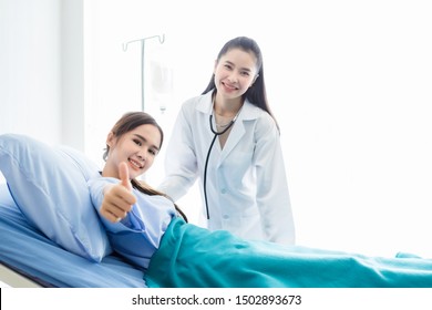 Asian Young Female Patient On Bed Showing Thumbs Up With Smiley Face Very Good Symptom To Asian Young Female Nurse Doctor In Hospital Background.