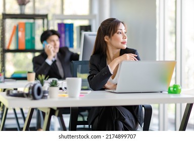 Asian young female professional businesswoman secretary employee in formal suit sitting at working desk typing report via laptop notebook computer while businessman manager work behind in office. - Shutterstock ID 2174899707