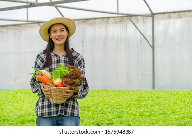 Asian Young Friendly Woman Farmer Smiling And Holding Organic Hydroponic Fresh Green Vegetables Produce Wooden Box Together In Greenhouse Garden Nursery Farm, Business Farmer And Healthy Food Concept