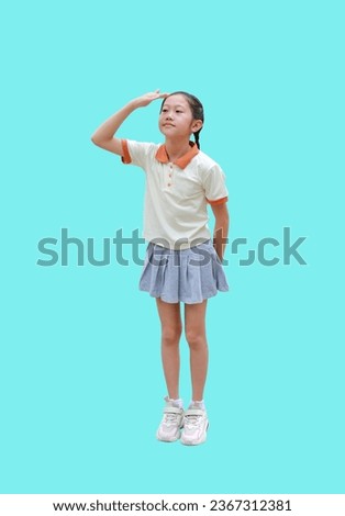 Asian young girl child holding hand above eyes and looking far away, expecting and searching something while standing isolated on cyan background. Image full length with Clipping path.