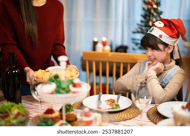 Asian young girl or daughter in a Santa hat smiles warmly as holiday dishes are served during a festive family Christmas dinner of reunion moment - Powered by Shutterstock