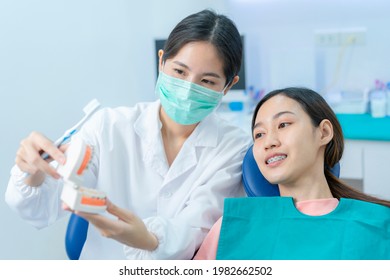 Asian Young Girl Listen To Female Dentist Explaining About Oral Care And Teeth Brushing For People Who Have Orthodontic. Orthodontist Wearing Protective Face Mask In Dental Clinic To Prevent COVID-19.