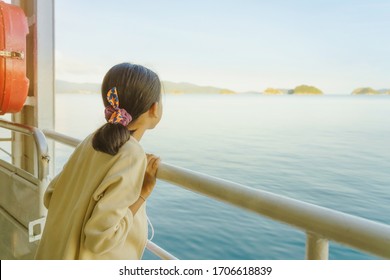 Asian young girl stands on baluster of ferry for relaxing and look at the ocean and island