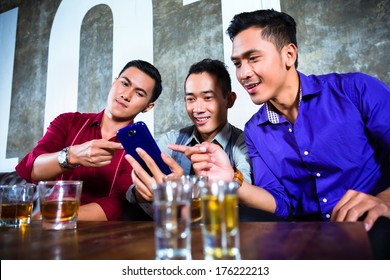 Asian Young And Handsome Group Of Party People Or Male Friends Looking At Smart Mobile Phone In Fancy Night Club