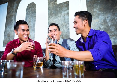 Asian Young And Handsome Group Of Party People Or Male Friends Looking At Smart Mobile Phone In Fancy Night Club