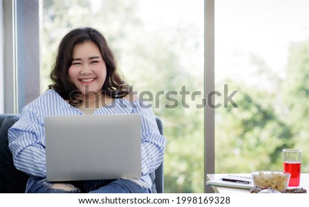 Asian young happy beautiful female model sit relaxing on sofa smiling look at camera using laptop computer work from home in quarantine time from covid pandemic moment.