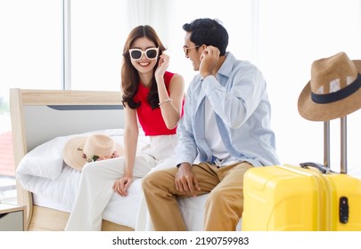 Asian Young Happy Male Female Traveler Lover Couple Husband Wife In Casual Outfit With Sunglasses And Hat Sitting Smiling On Bed In Bedroom Packing Luggage Ready For Summer Vacation Trip Together.