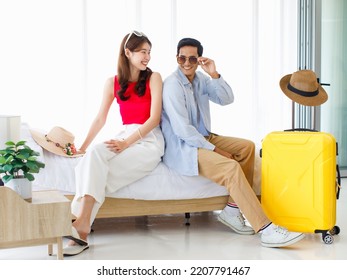 Asian Young Happy Male Female Traveler Lover Couple Husband Wife In Casual Outfit With Sunglasses And Hat Sitting Smiling On Bed In Bedroom Packing Luggage Ready For Summer Vacation Trip Together.