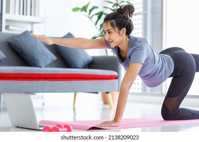 Asian Young Happy Peaceful Calm Healthy Female Model In Casual Sporty Outfit Smiling Doing Yoga Stretching Exercise On Mat Learning Studying Online Pilates Class Via Laptop Computer In Living Room.