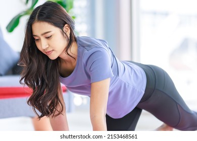 Asian Young Happy Peaceful Calm Healthy Female Model In Casual Sporty Outfit Smiling Doing Yoga Stretching Exercise On Mat Learning Studying Online Pilates Class Via Laptop Computer In Living Room.