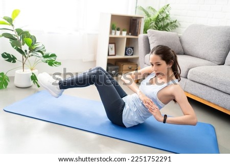 Asian young healthy woman exercising on yoga mat at home, she is doing a Russian twist.